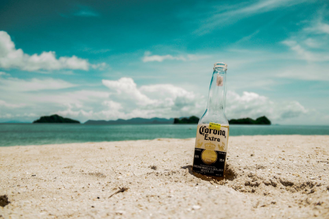 Sandstrand mit Corona-Bierflasche, im Hintergrund eine Insel